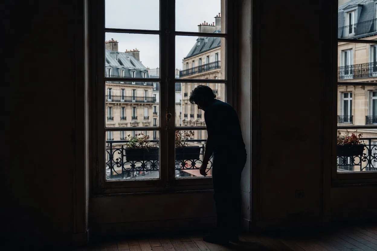 Silhouette pensive devant une fenêtre parisienne, ambiance de réflexion et d'introspection